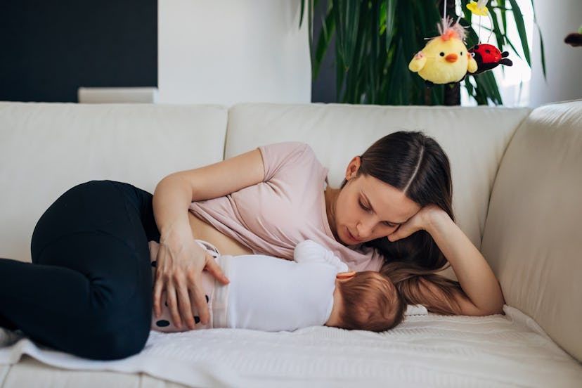 Mother lying down breastfeeding baby in a story about postpartum back pain exercises.