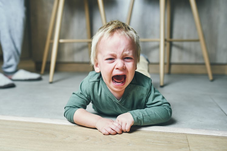 A little boy with blond hair, two years old, is lying on the floor and crying hysterically after kin...