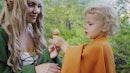 Fairy elf cosplay woman treats little baby boy hobbit with candy in green forest. Halloween concept,...