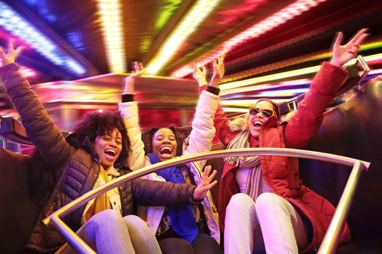 Three friends throw their hands up and laugh as they enjoy a ride at a fair during the luckiest day ...