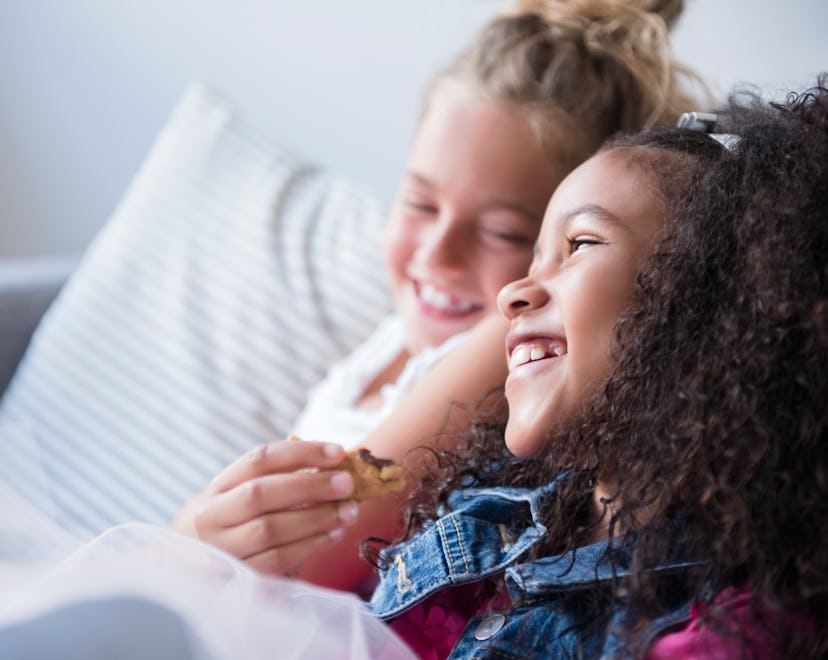 Two girls sitting together, smiling, having fun asking one another Would You Rather questions for ki...