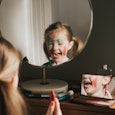 Cute young girl playing at a vanity table, applying various make up products.