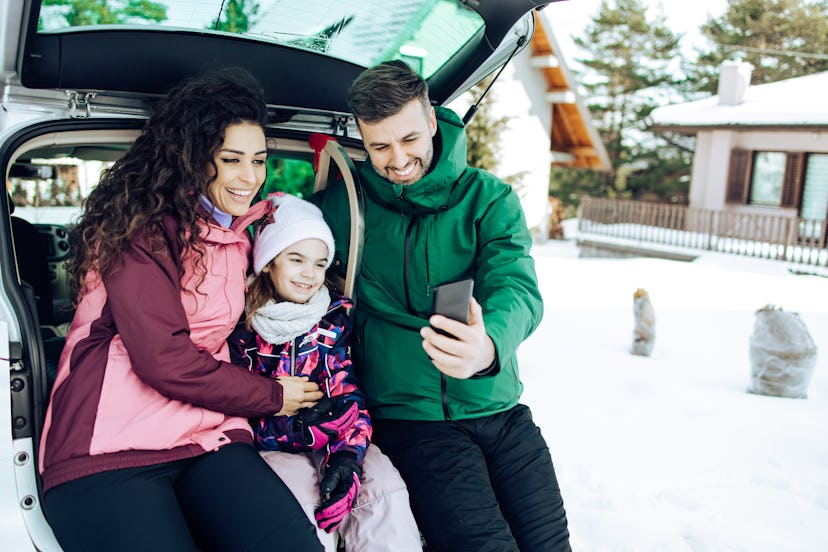Happy family packing suitcase and sleigh into the car trunk and preparing for their winter vacation.