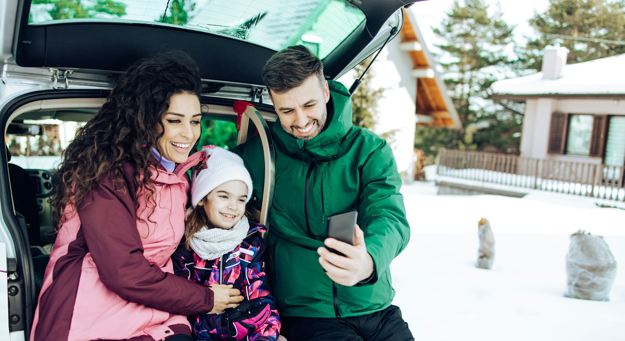Happy family packing suitcase and sleigh into the car trunk and preparing for their winter vacation.