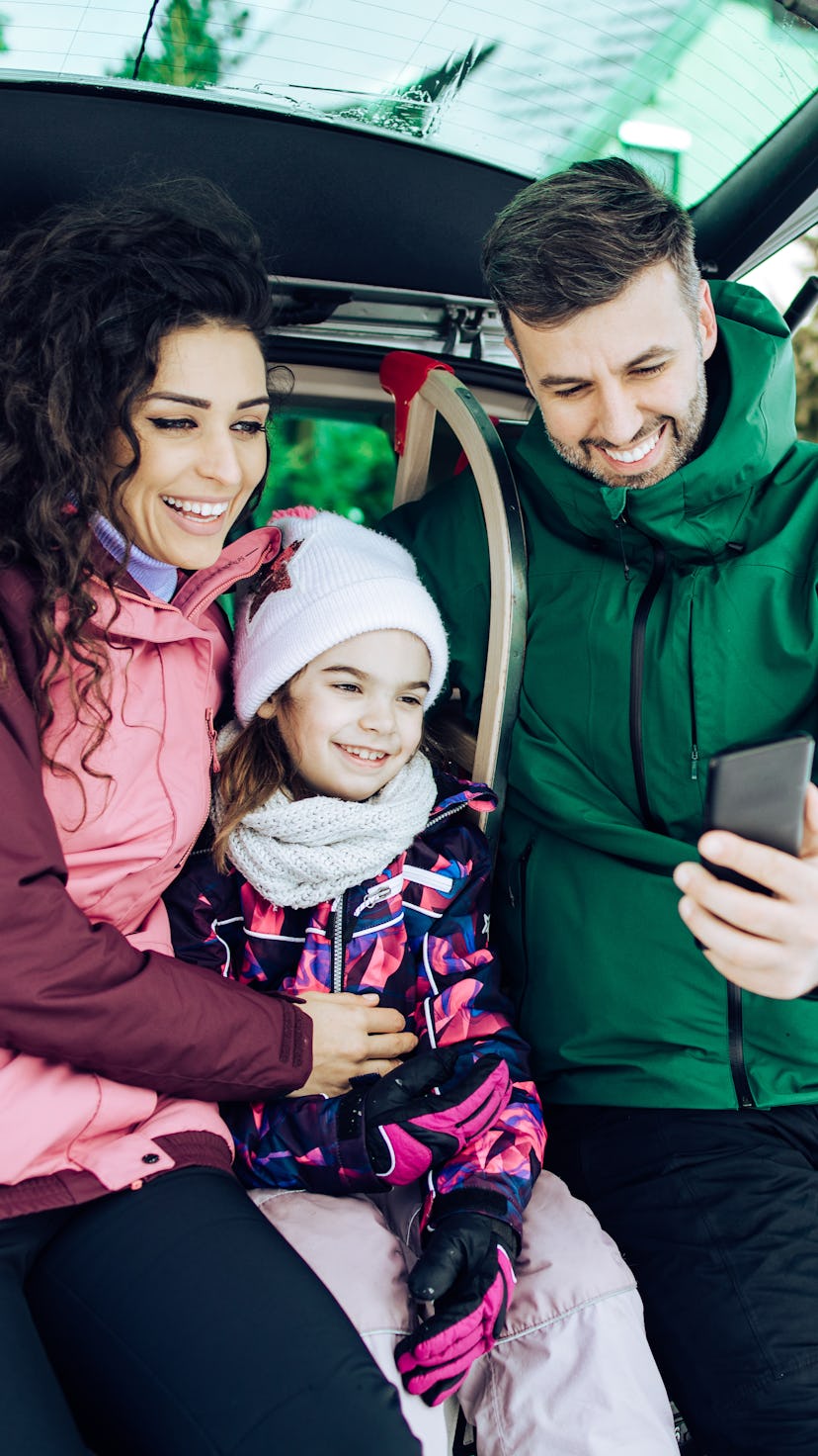 Happy family packing suitcase and sleigh into the car trunk and preparing for their winter vacation.
