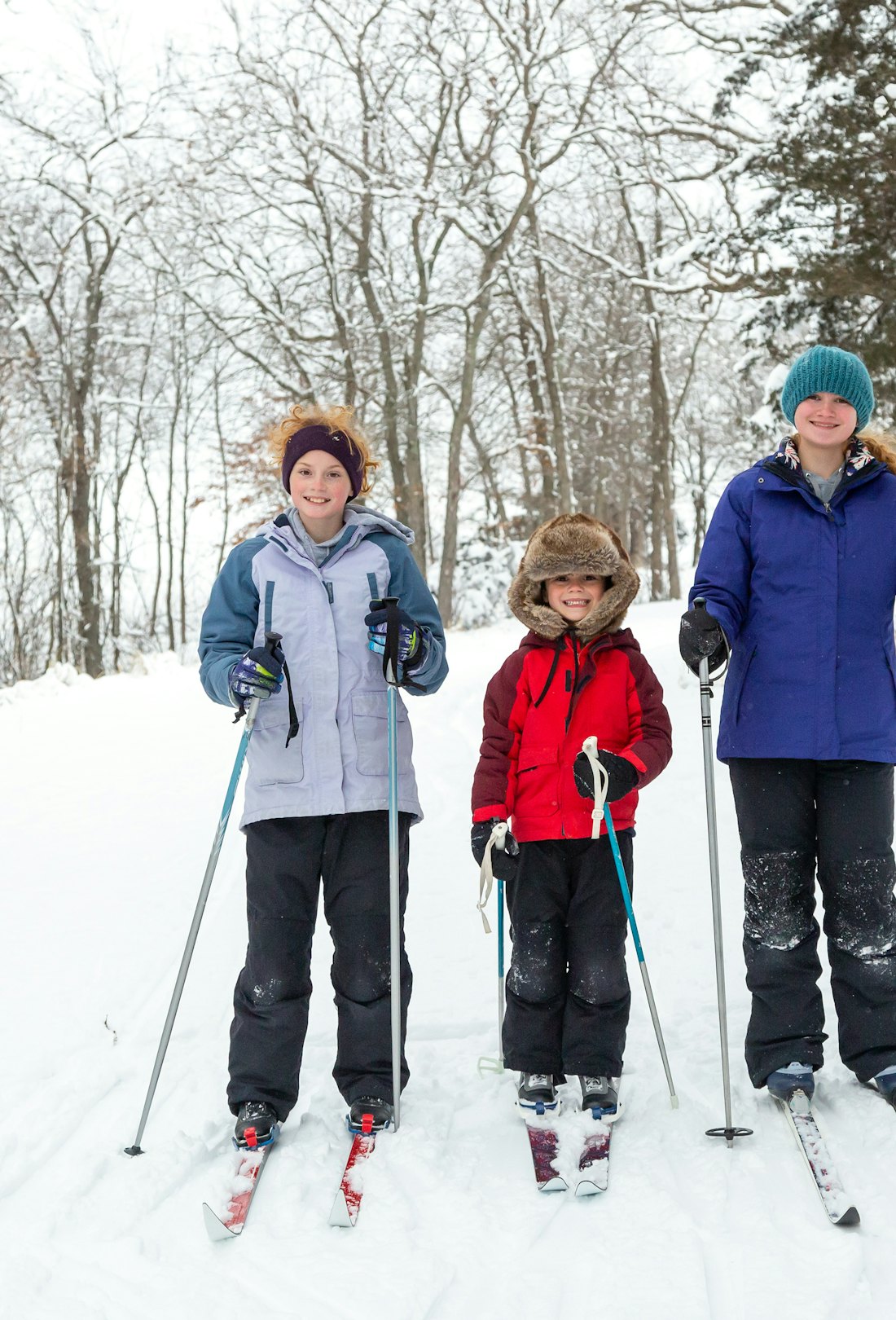 Two sisters and their younger brother stopping to smile for the camera while out cross country skiin...