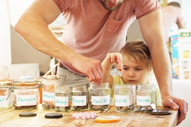 A dad and his child put coins in jars labeled for different expenditures.