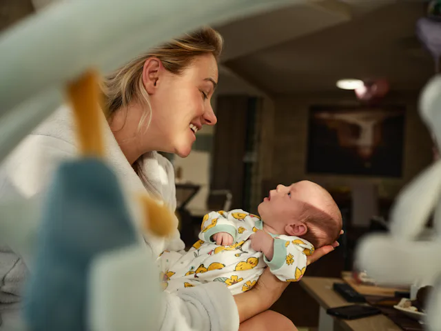 Happy single mother talking something to her newborn baby daughter at home.