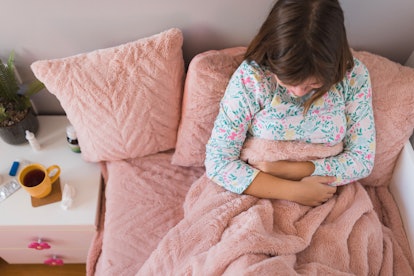 Girl in pajamas resting in bed when having a strong stomachache, appendicitis might be a cause for s...