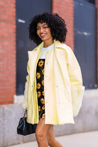 Yara Shahidi wears a balck floral sequin dress and a yellow puffer coat