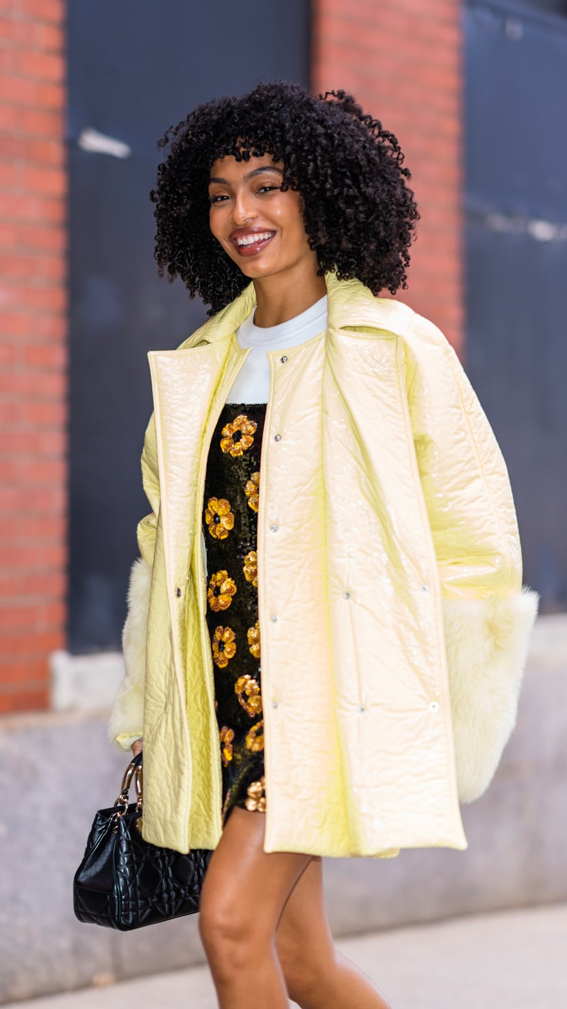 Yara Shahidi wears a balck floral sequin dress and a yellow puffer coat