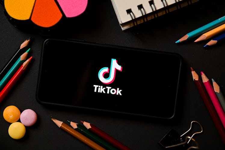 A smartphone with TikTok app on display on the desk full of pencils and notebooks.