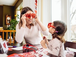 Mother and young daughter making greeting cards for Valentine's Day, surrounded by Valentine's Day d...