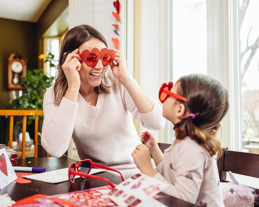 Mother and young daughter making greeting cards for Valentine's Day, surrounded by Valentine's Day d...