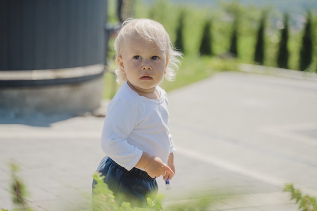 Little blonde boy walk at the backyard under the bush in an article about y names for baby boys