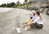 Barefoot mother and daughter bonding, sitting and drinking coffee, talking on rocky beach