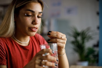 Copy space shot of young woman taking her medication. She is holding a glass of water and putting a ...