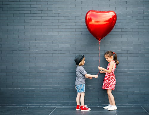 Two children with heart-shaped air balloon between them, exchanging Valentines in an article about V...