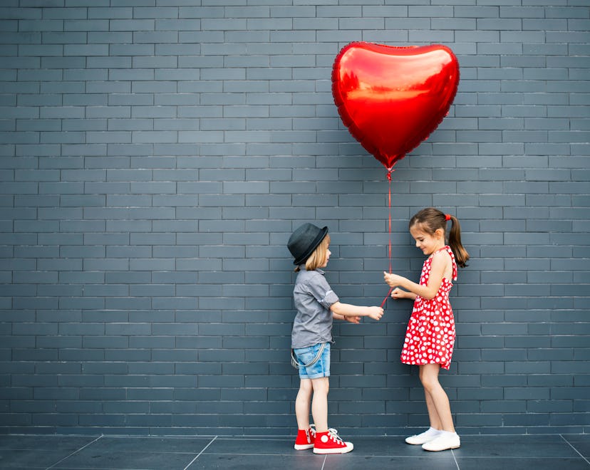 Two children with heart-shaped air balloon between them, exchanging Valentines in an article about V...