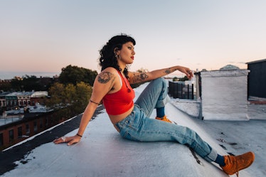 A young woman in a red crop top and jeans sits on a roof. The February monthly horoscope for every z...