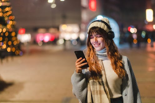 Young woman wearing headphones and using her smartphone. She is listening to music in the city at ni...