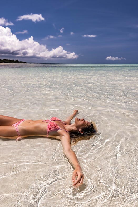 Happy woman sunbathing in shallow water during her summer vacation. Copy space.