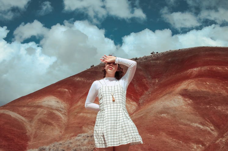 A young woman wearing a white dress with long sleeves and a short skirt shades her eyes while posing...