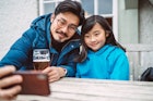 年轻英俊的爸爸和他可爱的女儿在酒吧花园享受啤酒时自拍。