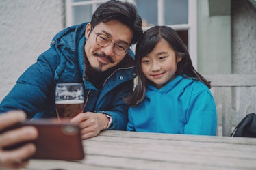 Young handsome dad taking selfie with his lovely daughter while enjoying beer in pub garden.