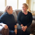 A mother and daughter sit on a sofa in their living room communicating with each other