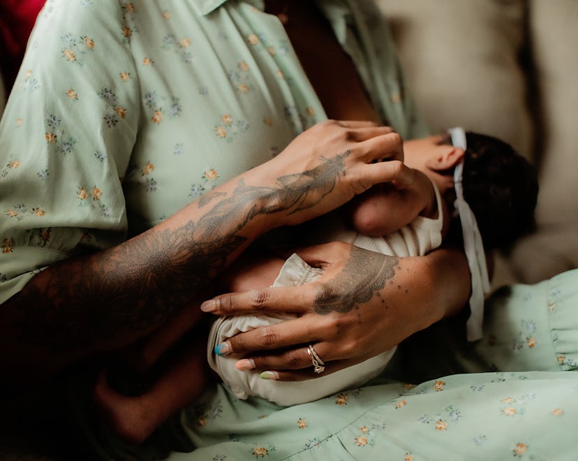 A breastfeeding mom holding a nursing baby with tattooed hands, showcasing an example of breastfeedi...
