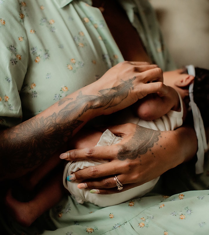 A breastfeeding mom holding a nursing baby with tattooed hands, showcasing an example of breastfeedi...