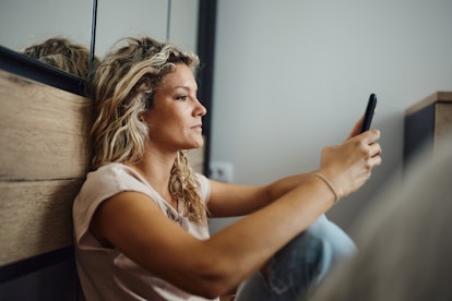 Profile view of young woman reading a text message on smart phone while relaxing at home. Emotional ...