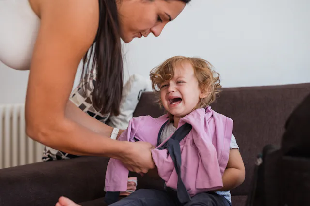 Young woman changing toddler girl, and the girl crying and shouting
