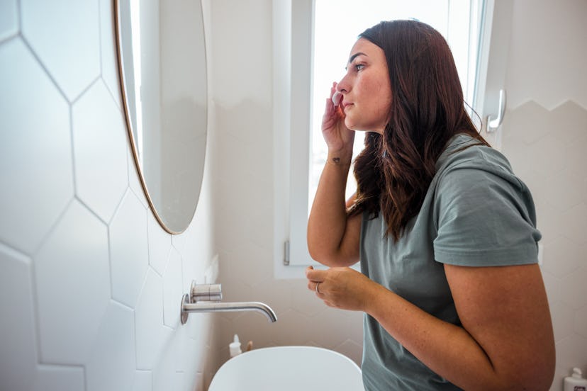 Young woman fixing her make up and taking care of her skin applying skin care cream