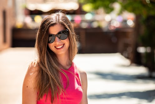 Portrait of young blonde girl with long hair and sunglasses smiling. Background of out of focus colo...