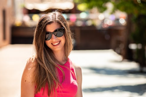 Portrait of young blonde girl with long hair and sunglasses smiling. Background of out of focus colo...