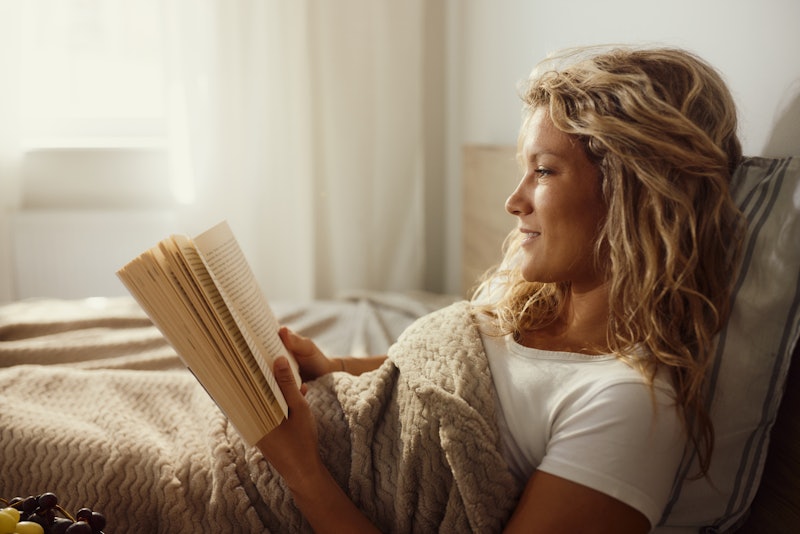 Young smiling woman reading a book during morning in a bed.
