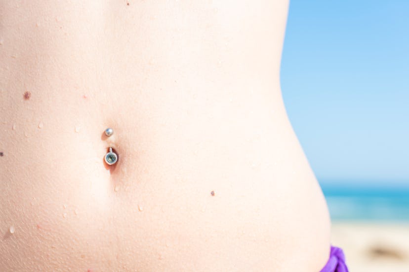 The beautiful abdomen of a woman on the beach with a bikini with a navel piercing