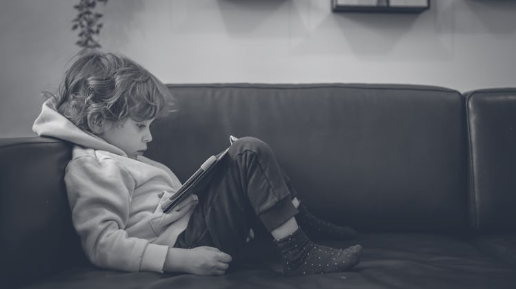 little boy, about 4 years old, sitting on the sofa, playing games with a digital tablet computer.