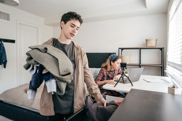 Brother is fixing clothes while sister is doing her homework with her laptop.