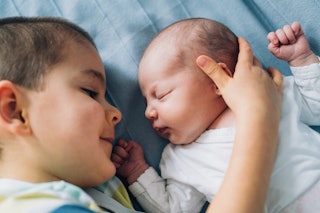 Cute little boy and newborn baby girl lying in the bed. Little brother hugging his newborn baby sist...