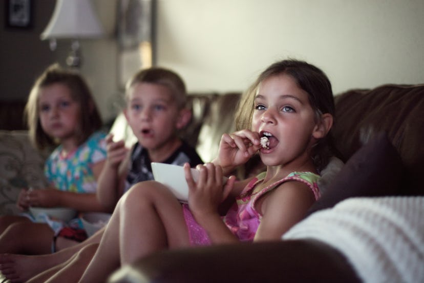 Children seated on leather couch, eating popcorn watching movie. popcorn choking hazard, can toddler...