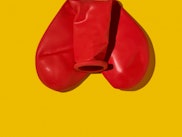 an uninflated red heart-shaped balloon folded resembling a penis and testicles on a orangish backgro...