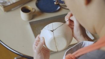 Woman repairing broken pottery at home. Kintsugi.