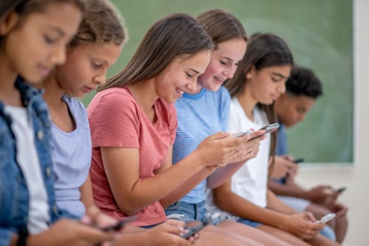 A multi ethnic group of teenagers who are high school students are busy with their phone in class.