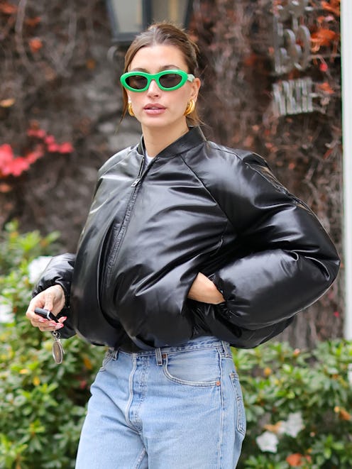 Hailey Bieber wears green sunglasses and a leather puffer coat.