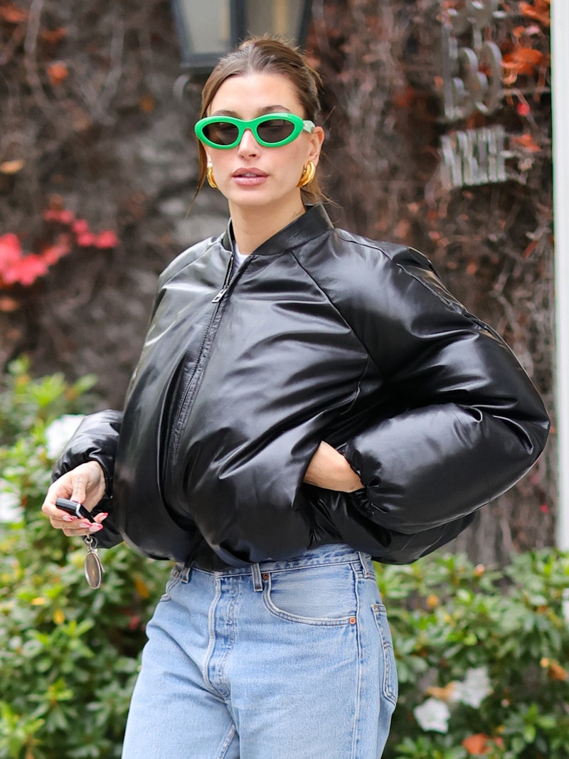 Hailey Bieber wears green sunglasses and a leather puffer coat.