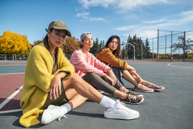 Three stylish women in streetwear lounge on a tennis court on a sunny fall day. as thThe January 202...