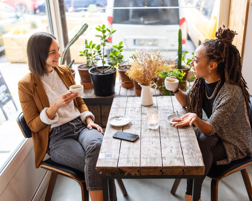 Two women strategizing and talking while drinking coffee, demonstrating how each zodiac sign makes N...